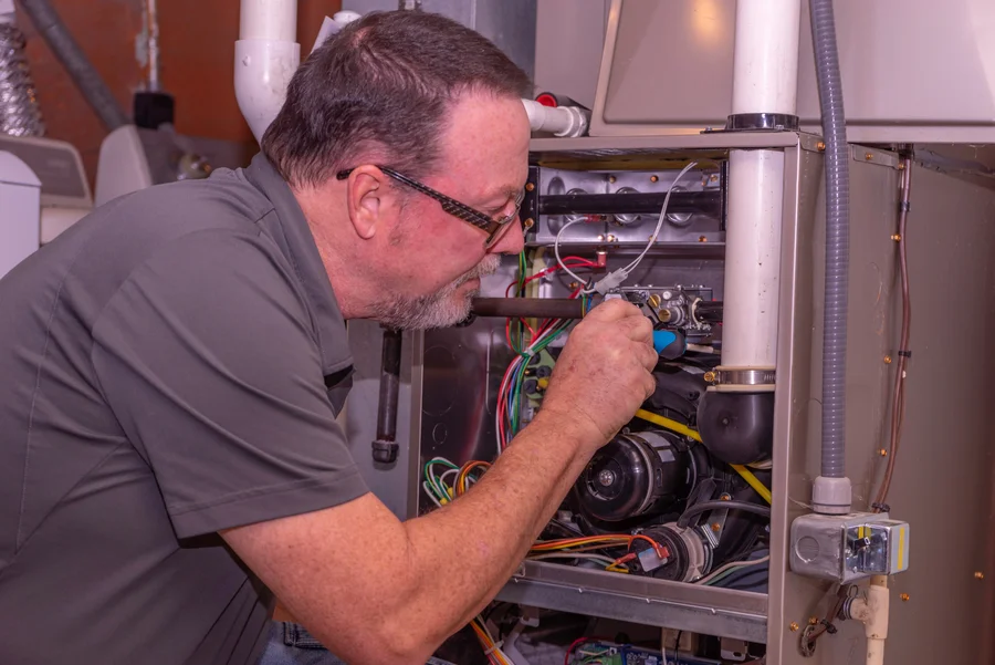 hvac-technician-inspecting-wiring-and-blower-inside-a-furnace-for-furnace-repair